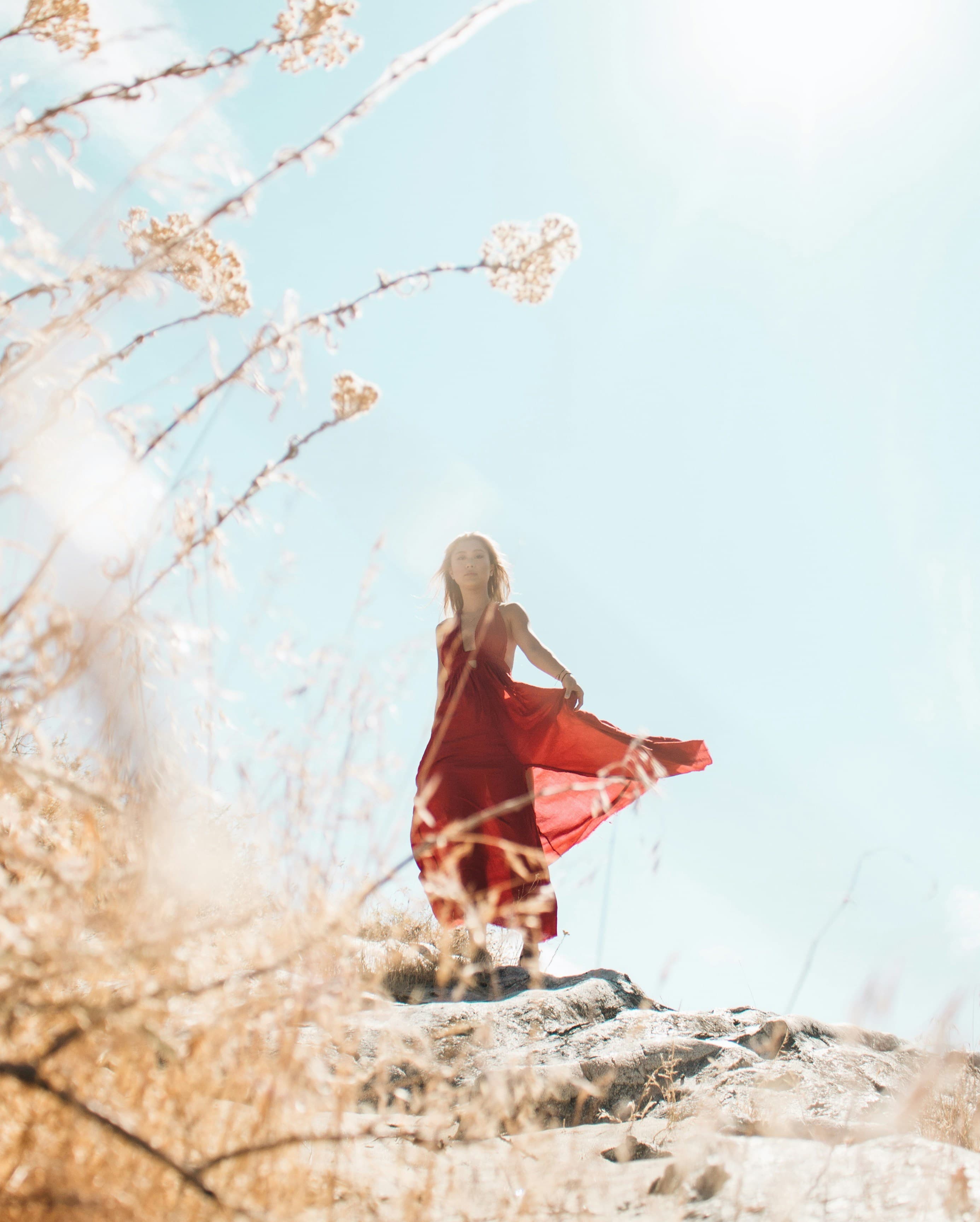 Woman in flowing red dress on landscape with confident, radiant expression